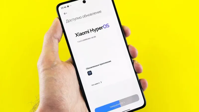Hand holding smartphone showing Xiaomi HyperOS update screen on yellow background.
