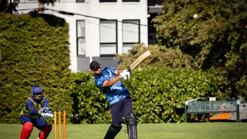 Cricketer hitting the ball with wicketkeeper ready during an outdoor cricket match.