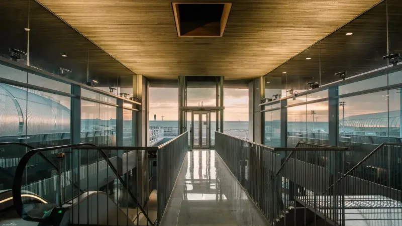 Un moderno corredor terminal del aeropuerto con paredes de vidrio, con vistas a la zona al aire libre al amanecer.