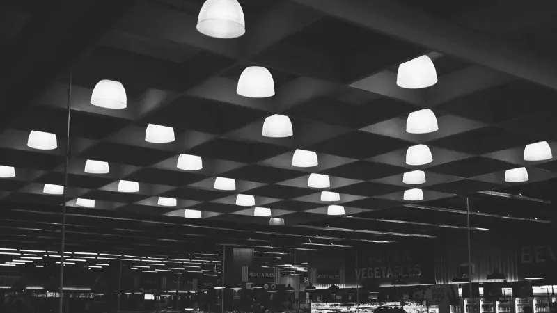 Black and white of rows of glowing lamps hanging over shelves with products in modern supermarket