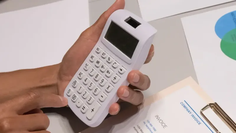 Close-up of hands using a calculator next to a company invoice, depicting a financial calculation concept.