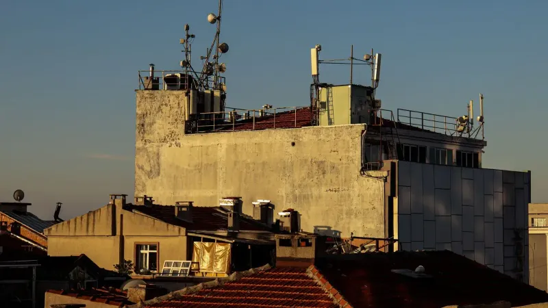 A city rooftop with antennas and relay towers against a clear blue sky at sunset.
