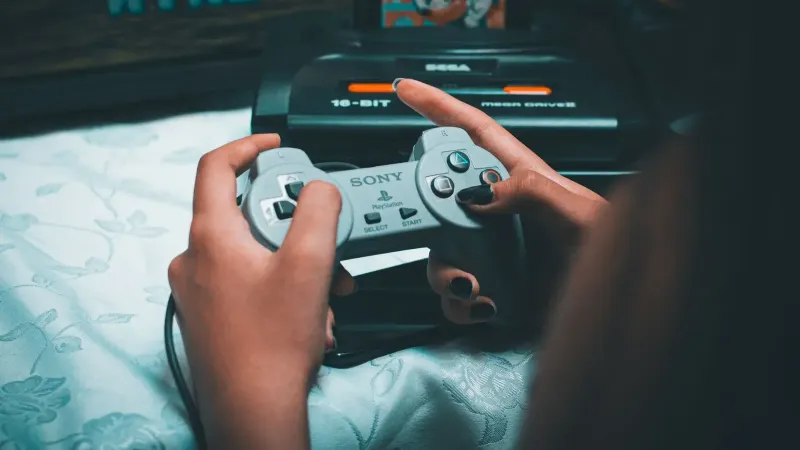 Close-up de manos sosteniendo el controlador Sony vintage con sega mega drive en segundo plano.