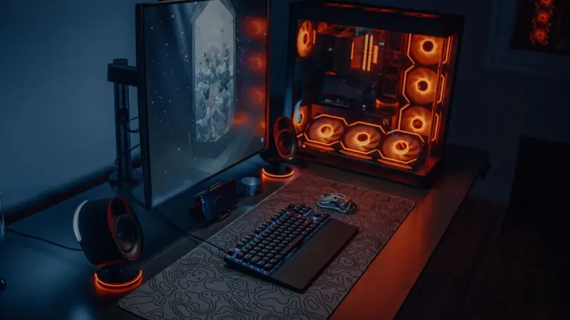 Sleek gaming desk setup featuring RGB lighting, large monitor, and gaming PC with glowing fans.