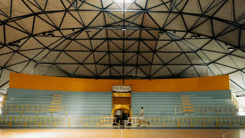 Un hombre corriendo por una cancha de baloncesto dentro de un pabellón deportivo con techo de cúpula.