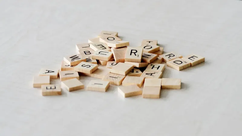 Primer plano de azulejos de letras de madera esparcidos sobre una superficie de mesa ligera, ideal para juegos de palabras.