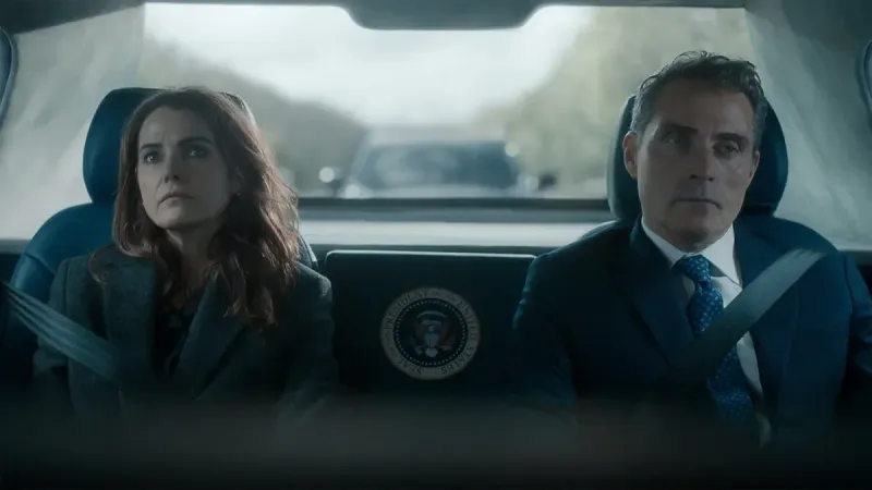 Dos personas serias, una mujer y un hombre con atuendo formal, se sientan uno al lado del otro en el asiento trasero de un automóvil con sello presidencial, usando cinturones de seguridad