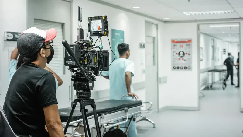 Cameraman capturing a scene in a hospital corridor with a professional video camera.