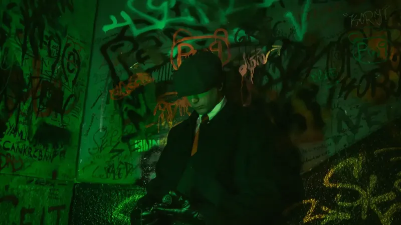 Stylish man in a trench coat and hat standing against vibrant graffiti wall, exuding retro elegance.