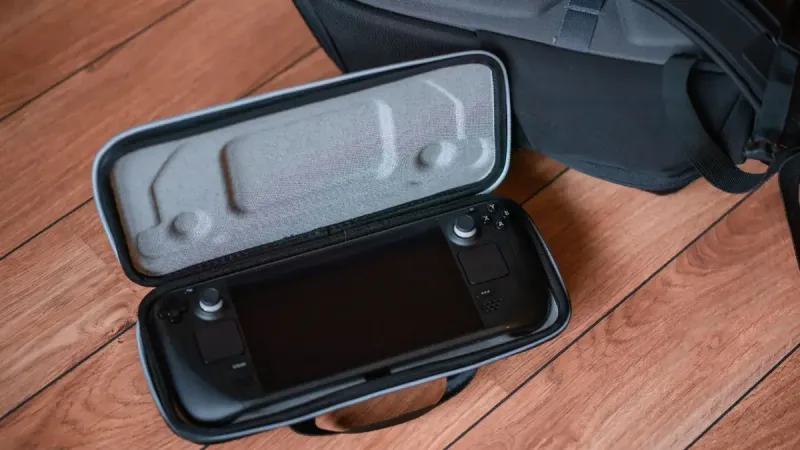 Una consola de juegos portátil en una funda protectora sobre suelo de madera con mochila.