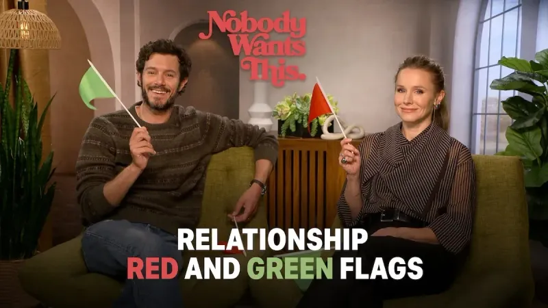 Adam Brody (Noah) y Kristen Bell (Joanne) se sientan en un sofá en una acogedora sala de estar, sonriendo y sosteniendo banderas verdes y rojas, con texto sobre "relación banderas rojas y