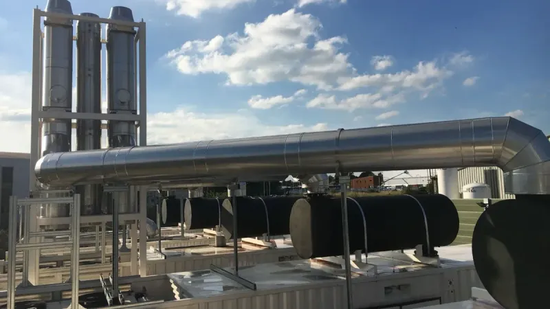 Modern industrial chimneys and support mast with flues against a clear blue sky, showcasing advanced infrastructure.