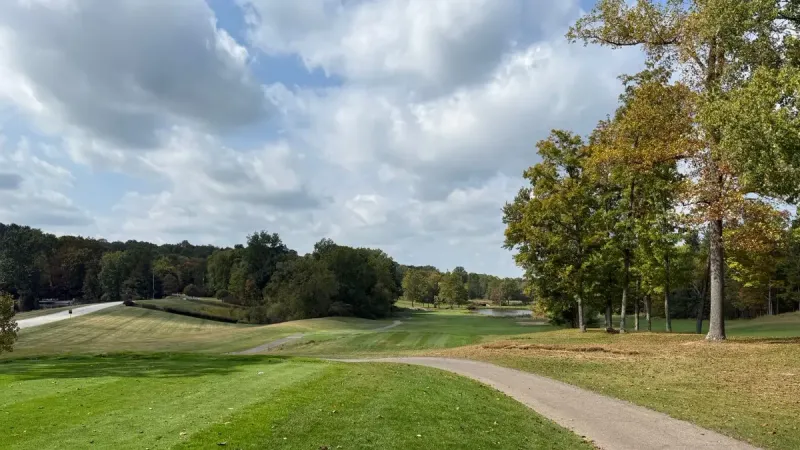 Hermoso campo de golf con exuberantes verdes y follaje de otoño bajo un cielo parcialmente nublado.