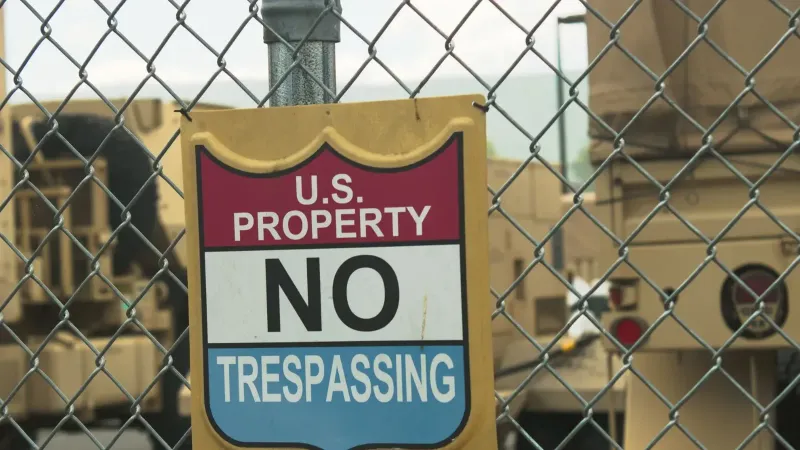 A no trespassing sign on a chain link fence at a U.S. property in Nevada with military vehicles in the background.