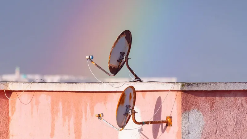 Two rusty satellite dishes on a rooftop against a vibrant rainbow in Tunisia.