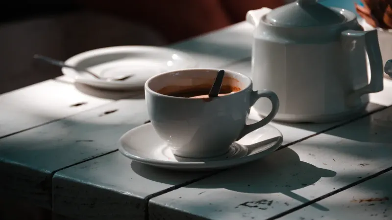 Taza de café blanco y olla sobre una mesa bañada por el sol, creando un ambiente acogedor.