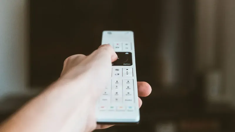 Primer plano de una mano usando un control remoto para operar un televisor en interiores.
