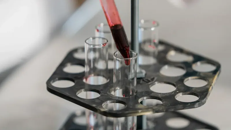 Red liquid being transferred into test tubes in a lab setting for research.