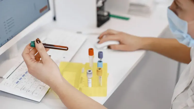 Trabajador médico analizando muestras en la computadora con tubos de ensayo cerca.