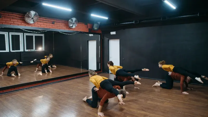 Grupo de bailarines ensayando coreografía contemporánea en un estudio de espejo.