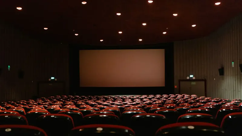 Un cine vacío con poca luz con filas de sillas rojas frente a una pantalla de proyector.