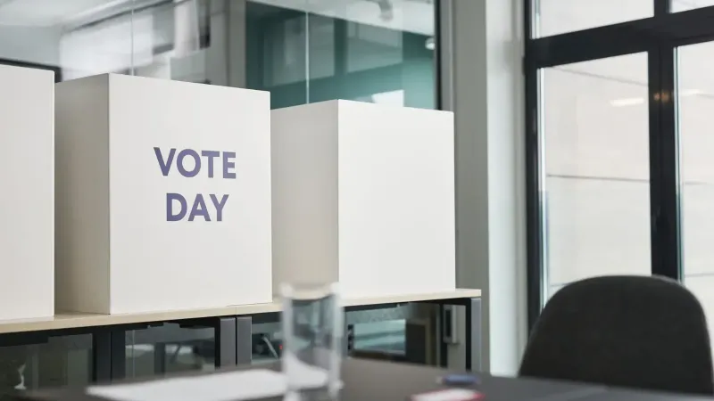 Una oficina moderna con cabinas de votación etiquetadas como "Día de votos" que indican actividad electoral.