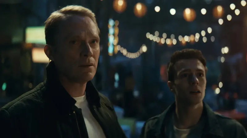 Visión y Tommy Maximoff están de pie lado a lado con expresión de preocupación y sorpresa frente a un fondo borroso de guirnaldas de luces en VisionQuest de Marvel