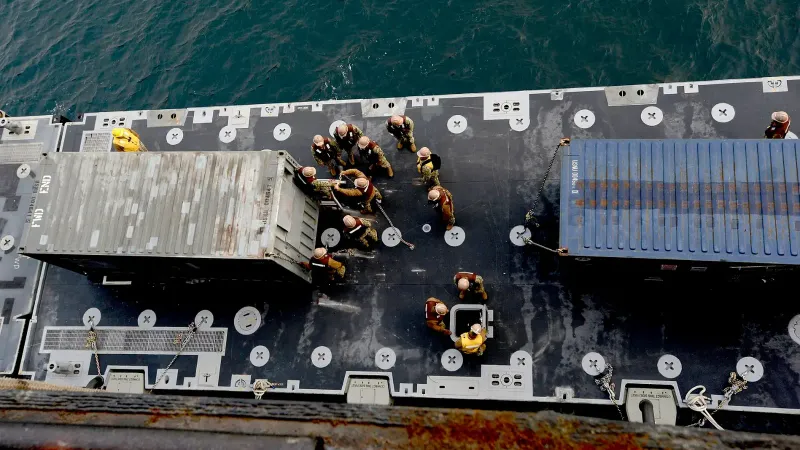 Los marineros estadounidenses con batallón de manejo de carga de la marina 1 aseguran un contenedor de transporte entregado desde el buque de carga del vehículo USNS Pililaau (T-AKR 304)