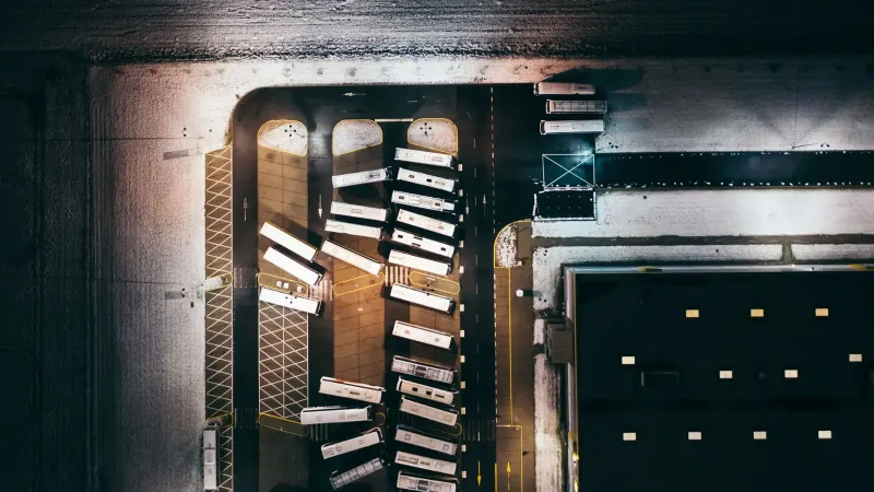 Perspectiva aérea de autobuses estacionados en un depósito cubierto de nieve por la noche, iluminado por luces artificiales.