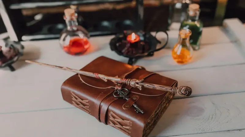 Un libro de hechizos vintage con una varita mágica y botellas de poción en una mesa rústica, evocando vibraciones místicas.