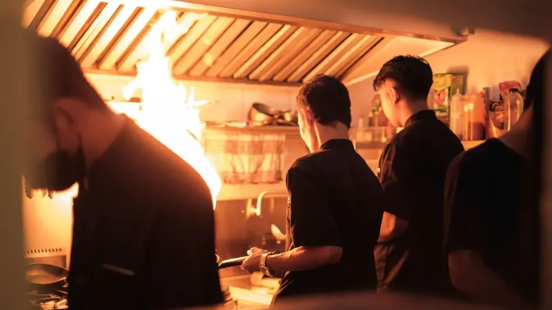 Chefs profesionales que trabajan en una cocina industrial ocupada con llamas visibles.